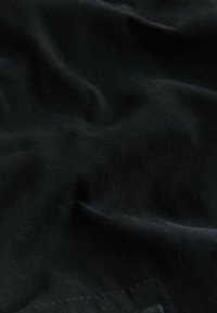 Detailný záber na mäkkú čiernu textíliu so subtílnymi záhybmi a jemnou textúrou, ktorá zobrazuje detaily tkania a drobné povrchové variácie.