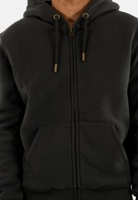 Veste à capuche zippée noire en tissu doux avec une grande poche avant, une capuche avec cordon de serrage réglable et des accents en métal doré.