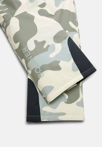 Camouflage skibroek in tinten groen, crème en marineblauw. Heeft een soepele textuur en een logo op het been. Ontworpen voor buitenactiviteiten.