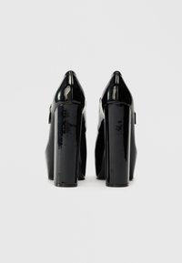 Zapatos de tacón alto de charol negro con punta afilada y diseño de tacón grueso, que presentan una textura suave y brillante.