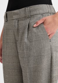 Grau karierte Hosen aus strukturiertem Stoff, mit taillierter Passform und Seitentaschen. Das Muster umfasst abwechselnde Karos und Hundstooth-Motive.