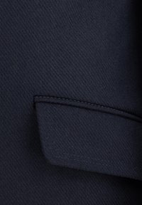 Granatowa tkanina wełniana w wzór jodełki; posiada złożoną kieszeń z kontrastowym przeszyciem oraz gładką fakturę.