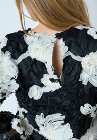 Melns auduma kleita ar baltām auduma ziedu apdrukām un reljefotu dizainu, atslēgu cauruma aizmugures aizdare un sarežģīti izšūti akcenti.