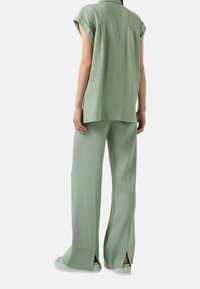 Persona che indossa una maglietta comoda a maniche corte di colore verde chiaro e pantaloni larghi con aperture posteriori, abbinati a sandali con plateau coordinati.