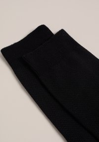 Čierne ponožky vyrobené z textúrovanej pleteniny s rebrovaným manžetom. Tkanina vyzerá jemne a je mierne elastická.