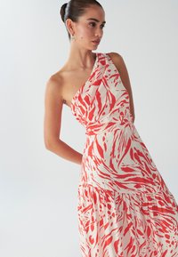 Ühe õlaga kleit punase ja valge abstraktse mustriga, millel on vöökoha kokkusurutud osa ja voolav seelik; valmistatud kerge kangaga.