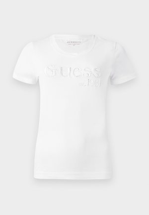 T-shirt en coton blanc à manches courtes, avec le mot "GUESS" en relief et "est. 1981" en impression contrastée. Texture lisse, col rond classique.