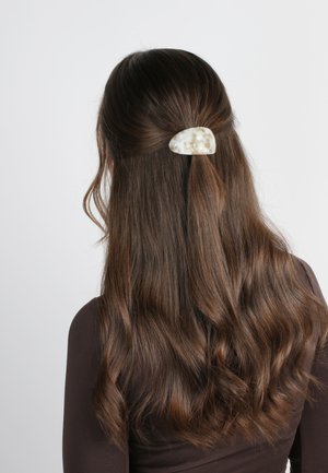 Fermaglio per capelli realizzato in materiale bianco traslucido con una finitura liscia e lucida; presenta una forma arrotondata e organica, posizionato in capelli castani mossi.