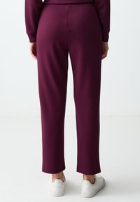 Bordeaux joggers van zachte stof, met een recht model, elastische tailleband en geribbelde boorden. Draagt met witte sneakers.