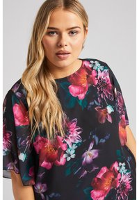 Blusa nera con vivaci motivi floreali in rosa, viola e verde. Maniche corte e scollatura rotonda con un tessuto leggero.