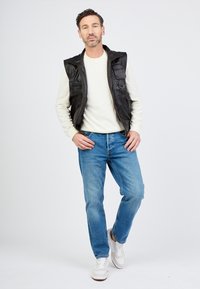 Svart läderväst över en ljusrandig långärmad skjorta, blå jeans och vita sneakers. Innehåller fickor på västen, avslappnad passform.