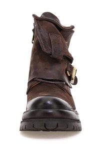 Stivaletto in pelle marrone con punta in gomma nera arrotondata, fibbia decorativa e parte superiore piegata. Dettagli in suede texturizzato e cucitura visibile.
