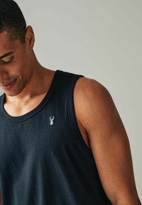 Sort tanktop lavet af bomuld, med rund hals og et lille broderet hjorte-logo på venstre bryst. Glat tekstur, ærmeløs design.