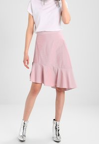 Jupe rose évasée avec un ourlet en volants, présentant un subtil motif rayé. Associée à un haut blanc et des bottines argentées brillantes.