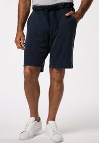 Marineblauwe shorts van zachte stof, met een elastische tailleband en een trekkoord, zijzakken en een relaxte pasvorm. Gepaard met witte sneakers.