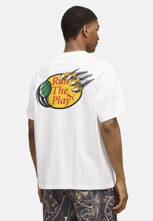 Mand iført en hvid t-shirt med en farverig grafik af en basketball, klo-mærker og tekst "Run The Play" på ryggen.