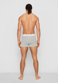 Šedé bavlnené boxerky s elastickým bielym pásom so značkou Calvin Klein, zobrazené zozadu, odhaľujúce priliehavý strih.