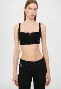 Black crop top made of denim with mesh paneling, featuring adjustable straps and front clasp. Worn with matching black jeans.