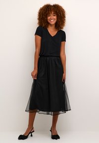 Rochie neagră cu un top moale de tricou, fustă fluidă din tulle și decolteu în V. Purtați cu pantofi cu toc slingback negri, cu accente în formă de fundiță.