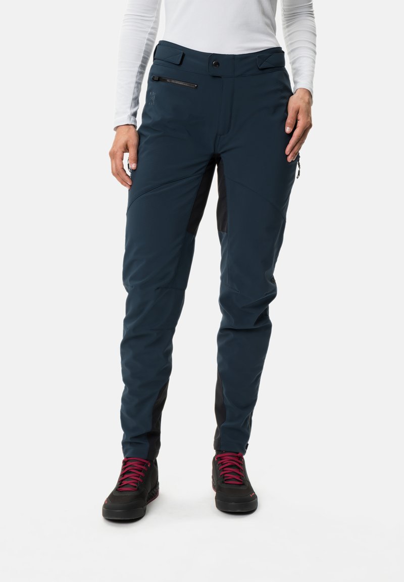 Pantalons d'extérieur bleu marine avec une coupe ajustée, accents noirs, poches latérales zippées et genoux renforcés, assortis à des bottes de randonnée noires.