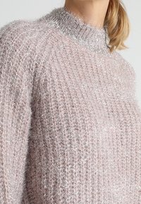 Jasnoróżowy sweter z dzianiny o teksturowanym, prążkowanym wzorze. Posiada delikatny kołnierz z srebrną nitką oraz miękki, puszysty materiał.