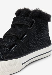 Black high-top sneaker with textured surface, featuring fuzzy collar, Velcro straps, and white rubber sole with black stripe.