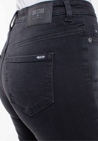 Jeans de mezclilla negra con una cinturilla alta, bolsillos traseros cosidos y una etiqueta con el nombre de la marca "BIG STAR" en la cinturilla.