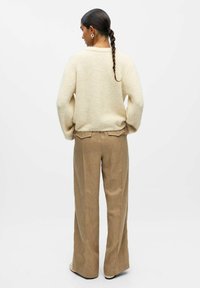 Beiger gestrickter Pullover mit langen Ärmeln, lockerer Passform und geripptem Saum, kombiniert mit hochgeschnittenen, hellbraunen weiten Hosen aus leicht strukturiertem Stoff.