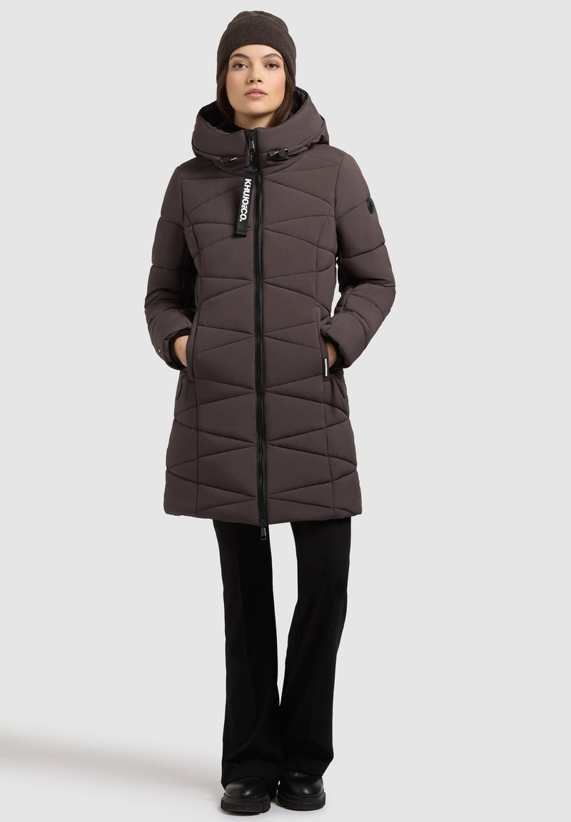 Giacca imbottita marrone con colletto alto, motivo a trapunta diagonale, zip nera e tasche laterali. Abbinate a pantaloni neri e stivali.