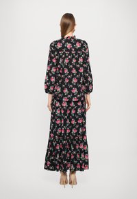 Blomstertrykk antrekk med svart bakgrunn, langermet bluse og maxi skjørt med lagdelt design. Innslag av rosa og grønn.