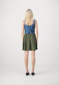 Denim anyagú felsőrész, olajzöld szoknyával, amely testhezálló felsőrésszel és bővülő aljjal rendelkezik, hátul pedig csat részlet díszíti.