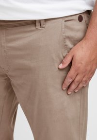 Beige cotton trousers feature a classic design with a smooth texture, front pockets, and a small brown brand patch on the waist.