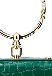Poignée circulaire en métal doré attachée à un fermoir de sac à main vert à texture crocodile sur fond blanc.