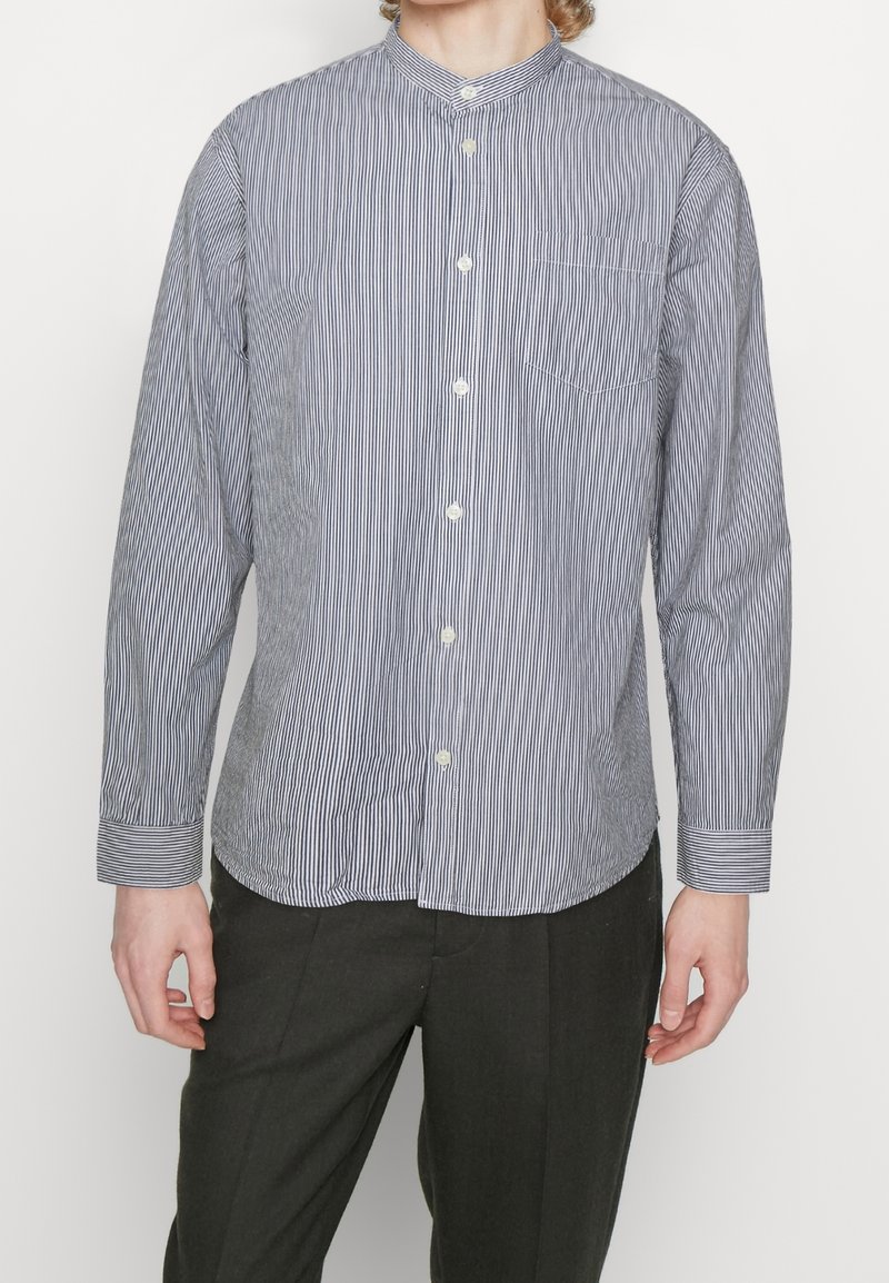 Gestreept overhemd in marineblauw en wit met een bandkraag, lange mouwen en een voorzak, gemaakt van lichte stof.