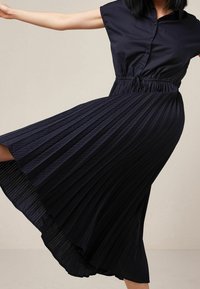 Marine siniväri plisseeritud kleit lühikeste varrukatega, nööpidega esiosa, elastse vöökoha ja tekstuurse kangaga. Midi pikkus voolava silueti jaotusega.