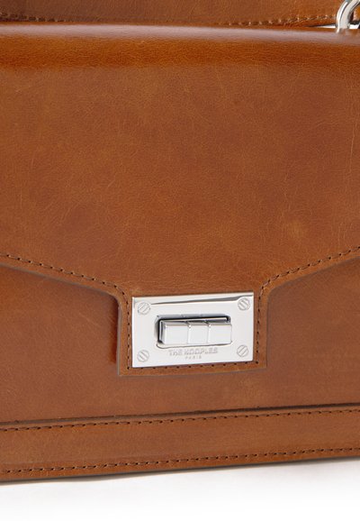 Borsa in pelle marrone con una consistenza liscia, caratterizzata da una chiusura in metallo argentato e marchio. Presenta dettagli cuciti e linee nette e angolari.