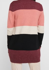 Lång cardigan i stickad kvalitet med djärva horisontella ränder i vinröd, rosa, beige och svart. Ribbad nederkant och ärmslut.