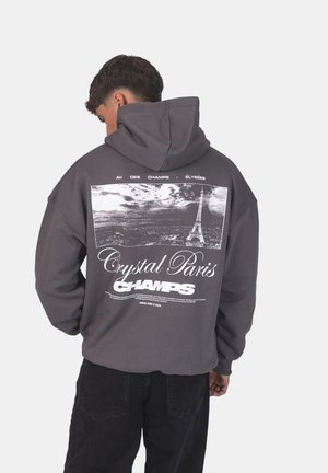 Grey hoodie with a large graphic print featuring the Eiffel Tower, text "Crystal Paris Champs," and black accents. Soft fabric, relaxed fit.