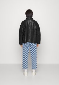 Sort læder oversized jakke med høj krave, parret med blå og hvide ternede bukser. Hvide sneakers fuldender looket.