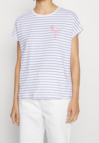 Camiseta blanca de manga corta con rayas horizontales azules y un bordado de flamenco rosa en el lado izquierdo del pecho. Corte relajado, tela suave.