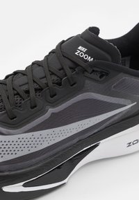 Baskets de course Nike Zoom noires avec tige en mesh texturé, accents gris et semelle rembourrée avec une bande blanche sur le bord.