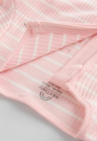 Vêtement pour bébé rose avec des rayures rose clair et blanches, texture côtelée et fermeture éclair. L'étiquette indique le nom de la marque "NEXT Baby" et les instructions d'entretien.