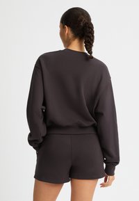 Felpa oversize grigia scura con maniche lunghe e scollo rotondo, abbinata a pantaloni corti coordinati; materiale morbido e leggero.