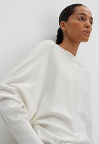Weißer, langärmliger Pullover mit lässiger Passform, gerippten Bündchen und glatter Textur. Verfügt über eine zentrale Naht, die vorne verläuft.