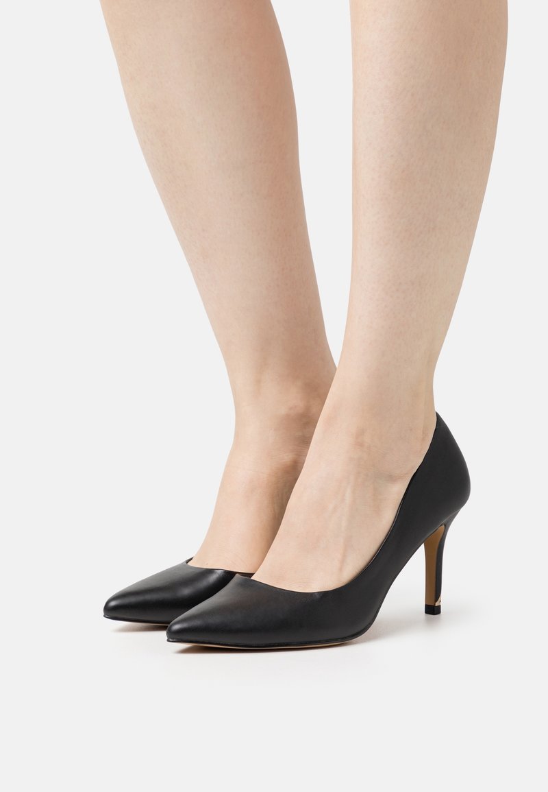 Escarpins noirs en cuir avec un bout pointu et un talon élancé. Texture lisse, design minimal, et une légère découpe sur les côtés.