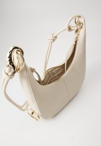 Beige leather handbag with a curved shape, gold hardware accents, and a zip closure, featuring thick, knotted straps.