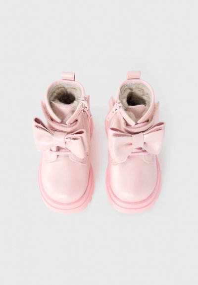 Bottes de cheville en cuir rose avec une finition brillante, dotées d'un grand nœud à l'avant, d'un doublure en peluche et d'une épaisse semelle en caoutchouc rose.
