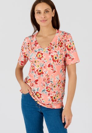 Camiseta de cuello en V floral en color coral con mangas cortas. Presenta una mezcla de grandes flores rojas, amarillas y azules sobre un fondo texturizado.