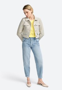 Lys grå tweedjakke med to forlommer, gul top og lyseblå afslappede jeans. Beige flade sko fuldender outfittet.