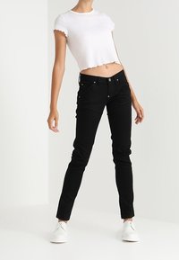 Bílé zkrácené ribbed tričko v kombinaci s černými slim-fit džíny. Oblečení doplňují bílé boty. Jednoduchý design, čisté linie.